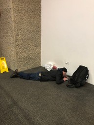 Man lays on his stomache charging his mobile phone.