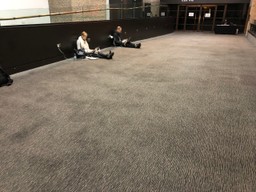 Three people sit on the floor with laptops in a large hallway. A staff member at the back doesn't look bothered.