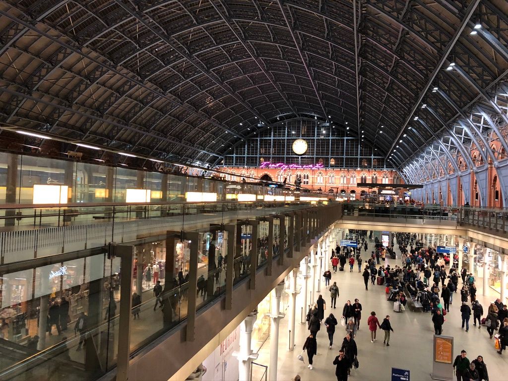 A busy train station, huge arched ceiling, shops and travellers below.